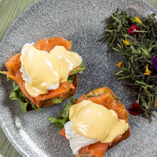 Open-faced toast with smoked salmon, poached eggs and hollandaise, served with a side of mixed greens.