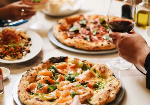 A group is dining together with pizza on the table and glasses of red and white wine.
