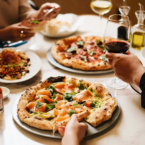 A group is dining together with pizza on the table and glasses of red and white wine.