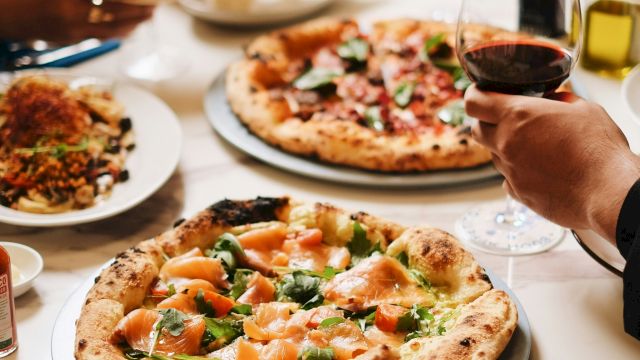 A group is dining together with pizza on the table and glasses of red and white wine.