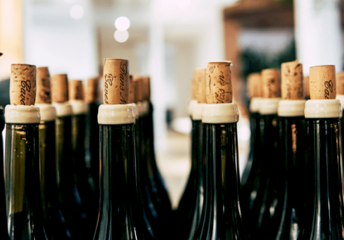 A close-up of dark green glass bottles lined up in rows with corks and white caps, likely champagne or wine bottles.